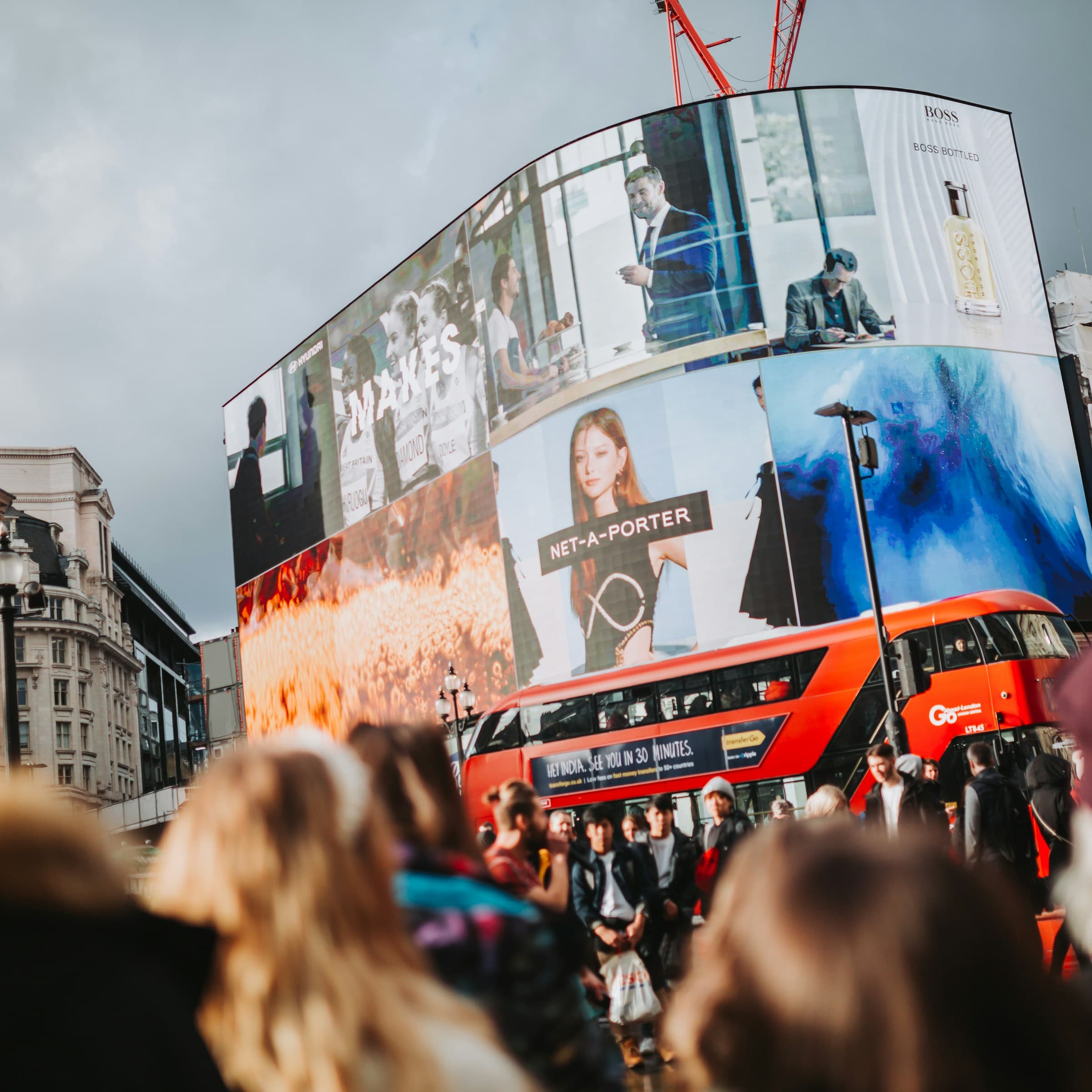 Curved advertising billboards above a red double-decker bus at Piccadilly Circus, London.